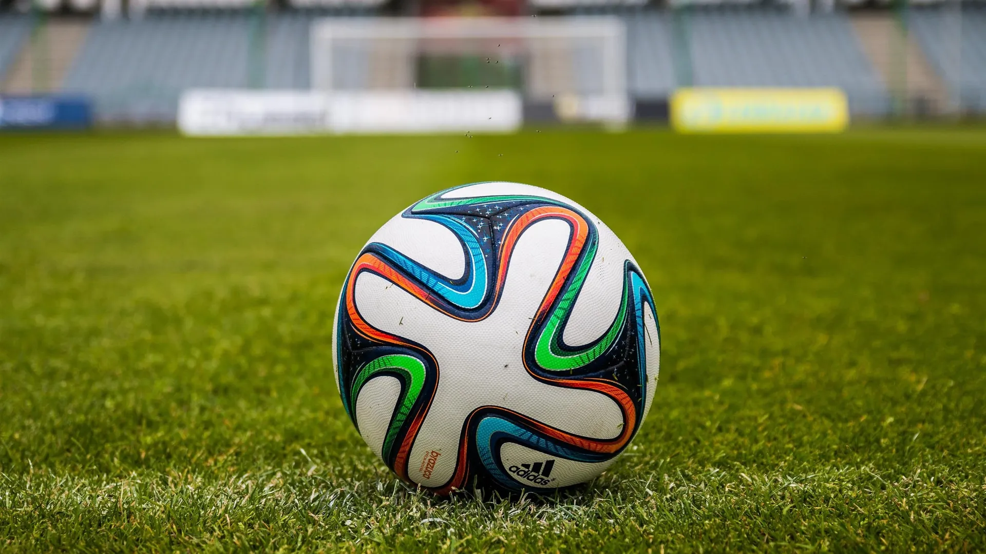 Stadion klubu sportowego z magazynem sprzętu treningowego w tle, etykiety inwentarzowe na piłkach, strojach i wyposażeniu treningowym podczas spisu z natury